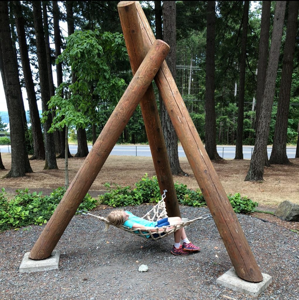 a kid relaxing in a hammock attached to three large poles in a teepee shape