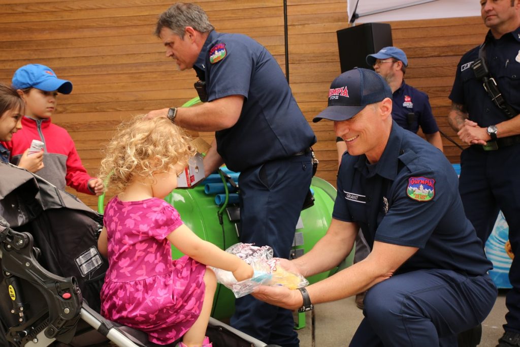 a little girl reaches to take a treat from a bag a fireman is holding