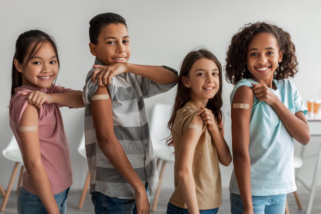 Cheerful Vaccinated Kids Showing Arms After Covid-19 Vaccination Smiling To Camera Posing Indoors. Multicultural Children Group Standing After Receiving Their Vaccine. Coronavirus Immunization