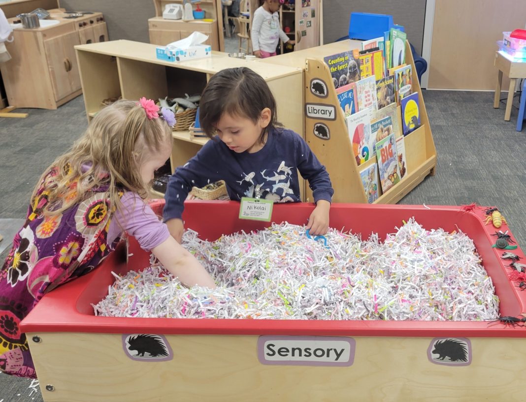 two kids play in a sensory bin full of paper shreds