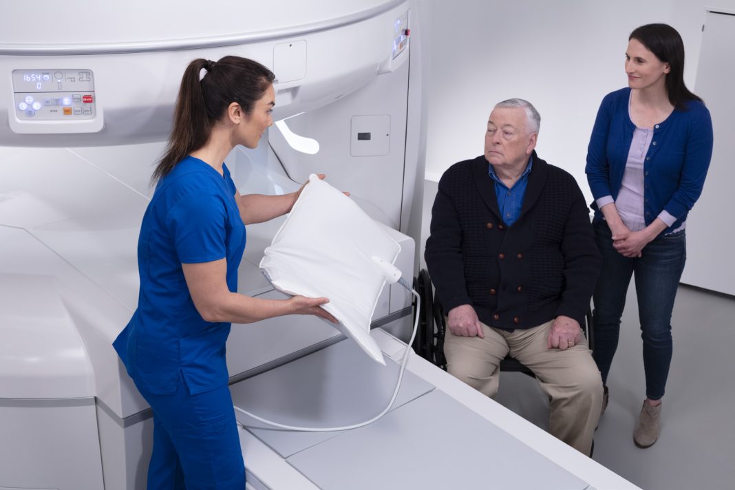 a doctor talking to a male patient with a woman standing next to him with the MRI machine between them