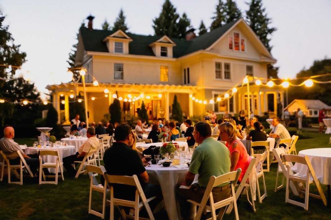 Schmidt House with twinkle lights and people sitting at large round tables on the lawn with white tablecloths.