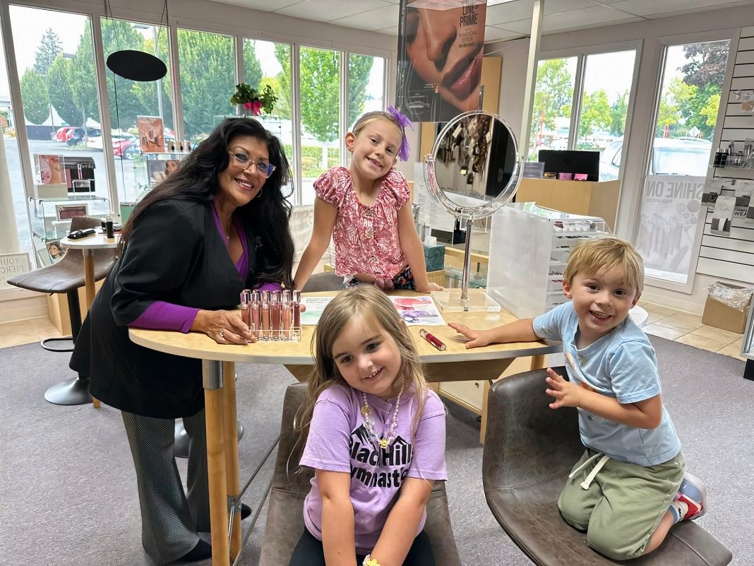 a woman and three kids site around a make up counter