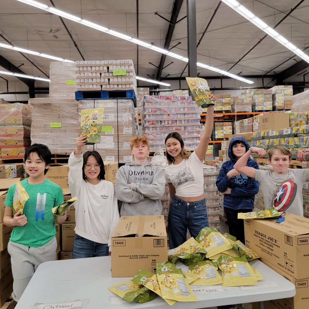 middle school students posing for a photo at a food bank, a few are holding up bags of food