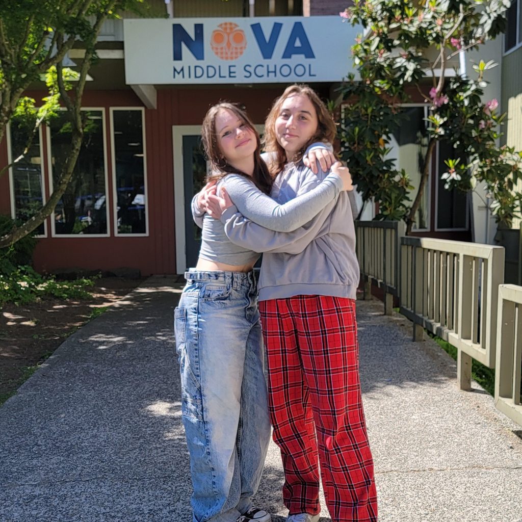 Two girls hugging by the NOVA Middle School Sign