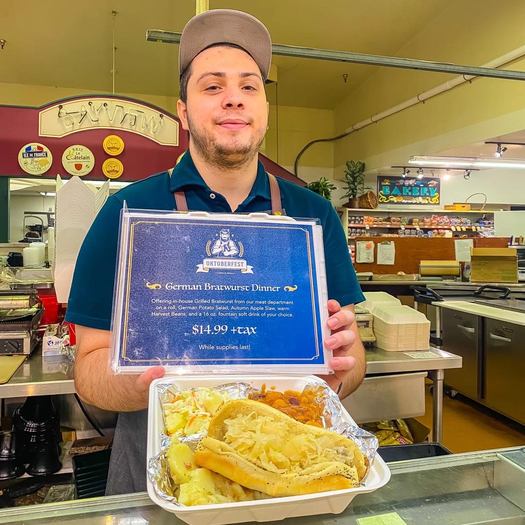 bayview worker holding a to go container with a bratwurst and potatoes in it.