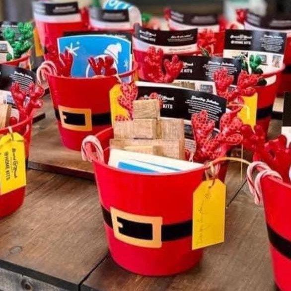 santa themed buckets with craft supplies, a candy cane and red felt reindeer antlers in them