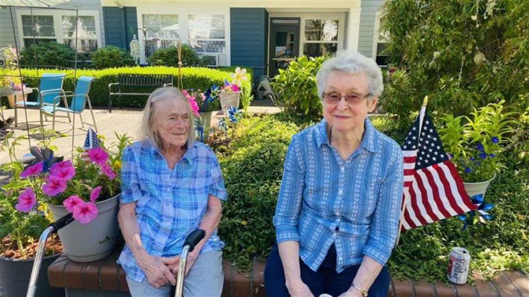two senior citizens sit on a bench outside