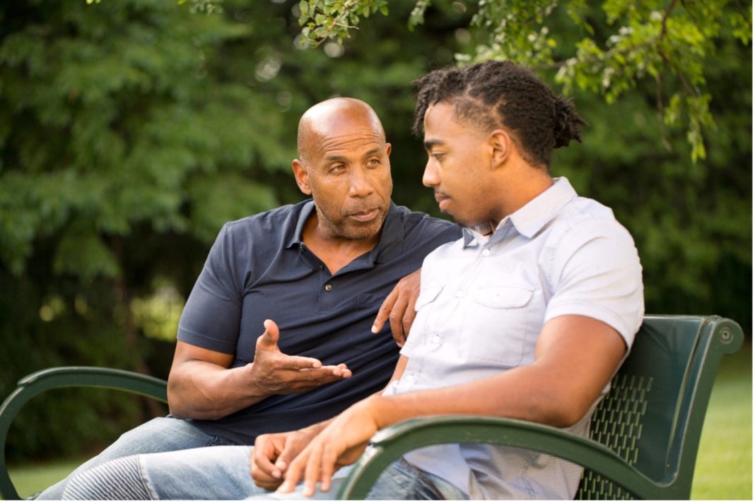 two men talking on a bench outside