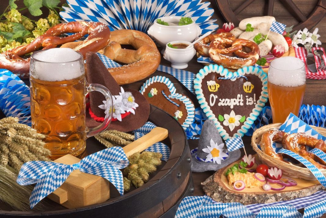 All typical German Bavarian symbols in one picture. Gingerbread heart with „The beer is tapped“ text, soft pretzels, Bavarian veal sausage and beer.
