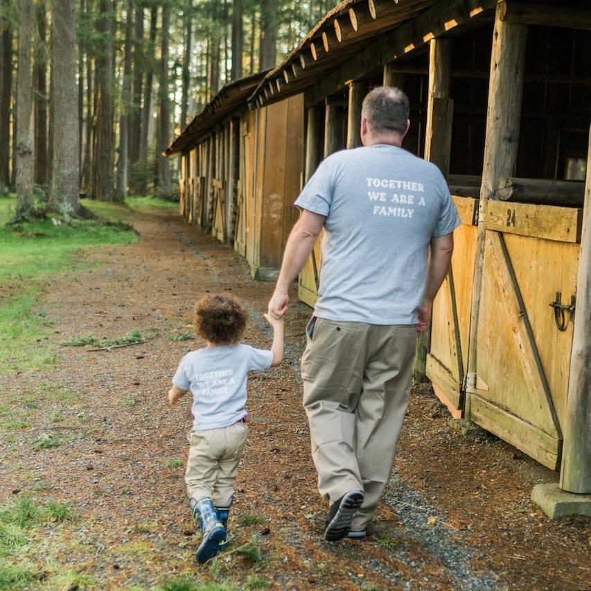 a man holding a young boy's hand walking away from the camera along a barn