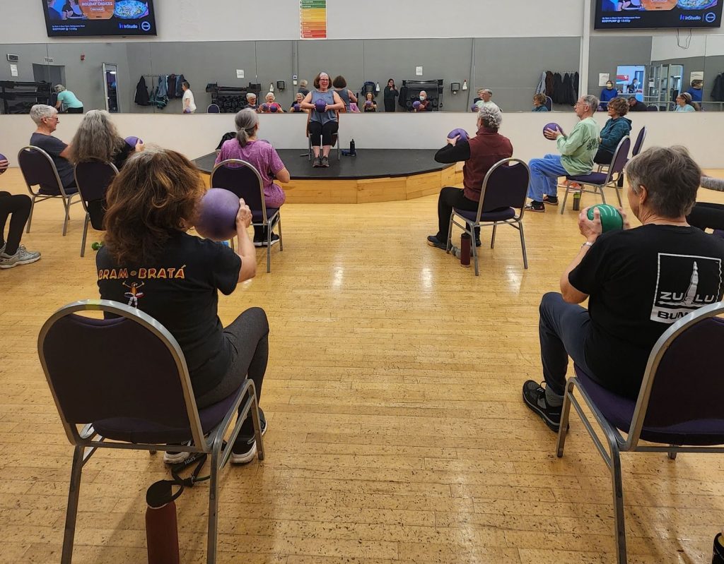 people in chairs in a gym holding exercise balls