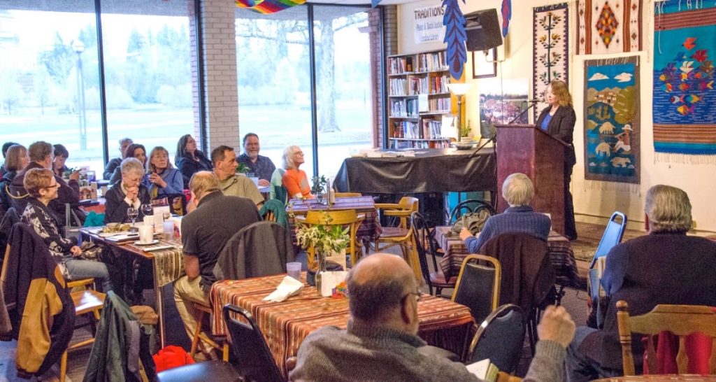 a large group of people sitting at tables listening to poetry