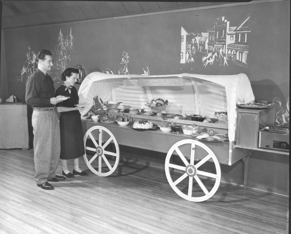 black and white photo of people in a buffet line that looks like a covered wagon