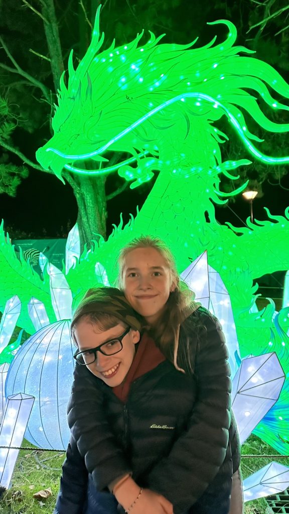two girls hugging in front of a holiday light display
