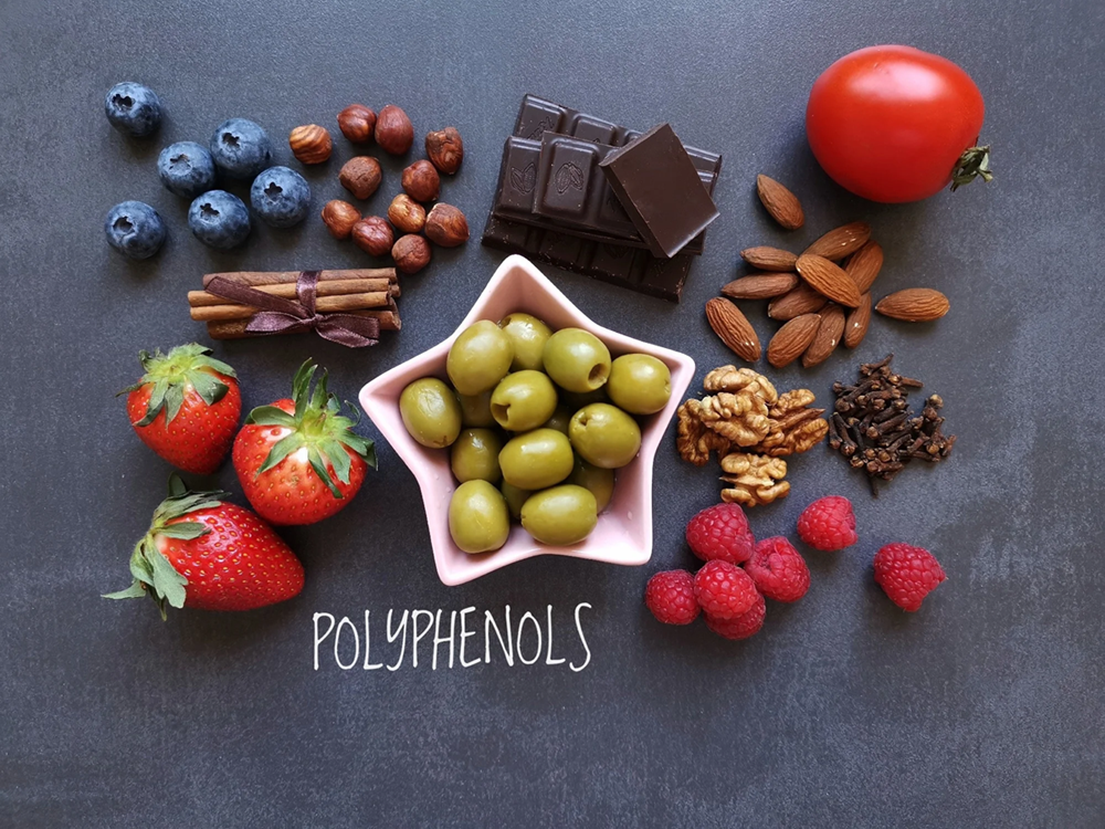 strawberries, hazelnuts, cinnamon sticks, blueberries, almonds, walnuts, raspberries green olives and a tomato, gray background