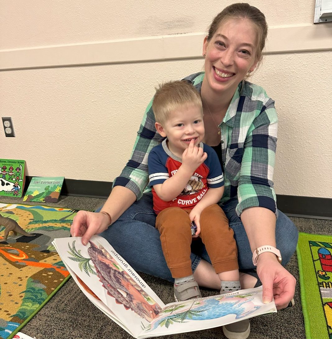 a woman sits on the floor with a kid on her lap reading a book