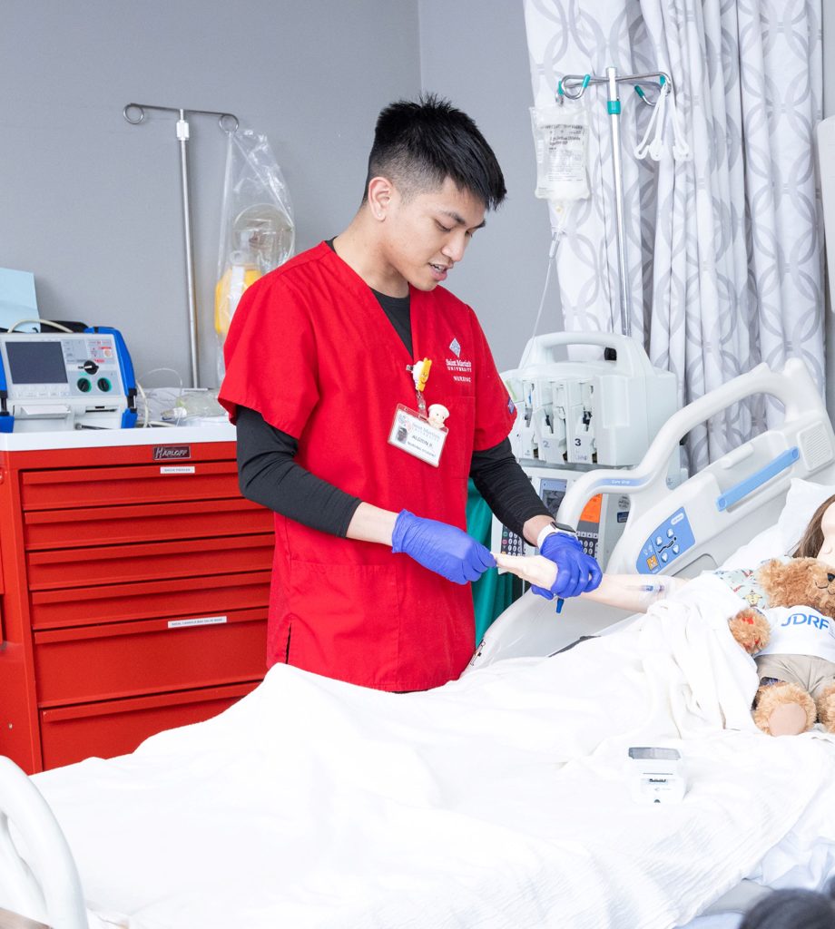 Saint Martin's University Nurse student checking the hand of a fake mannequin patient in a hospital bed