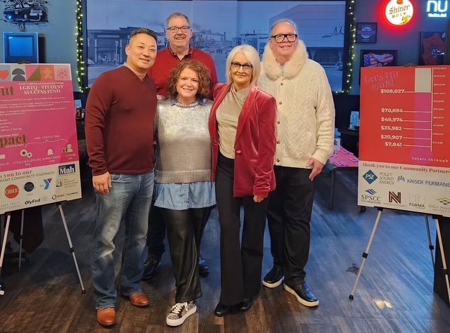 Four people smiling and standing between two posters showing Community partner logos.