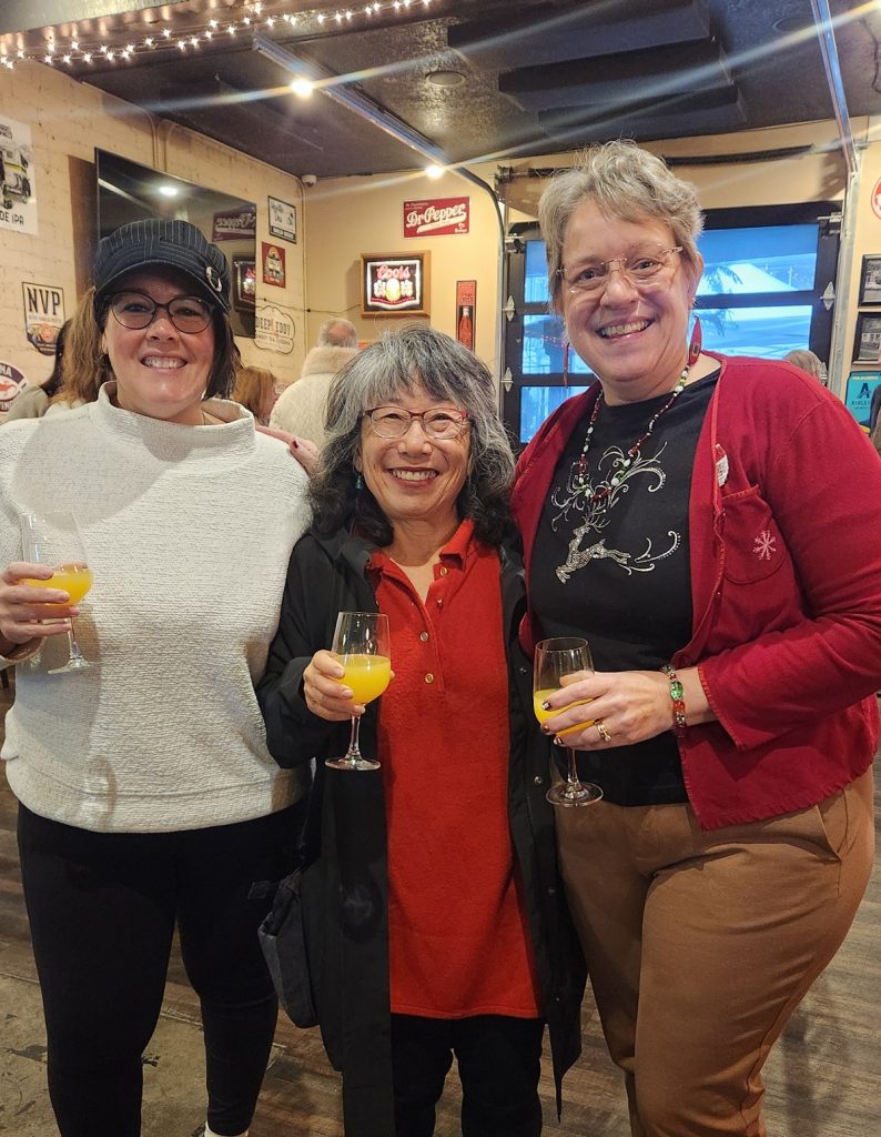 Three people smiling and holding beverages in Nicole’s Bar.