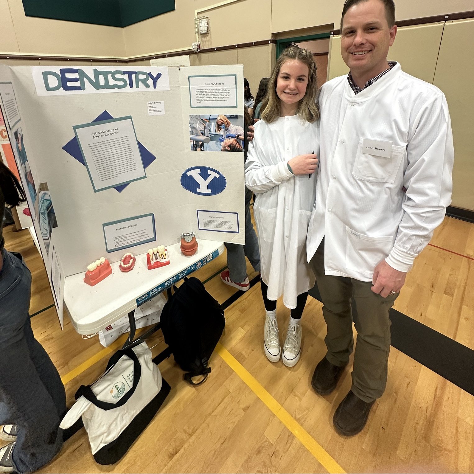 a young girl and her dad dressed as dentist stand next to a Dentistry project board