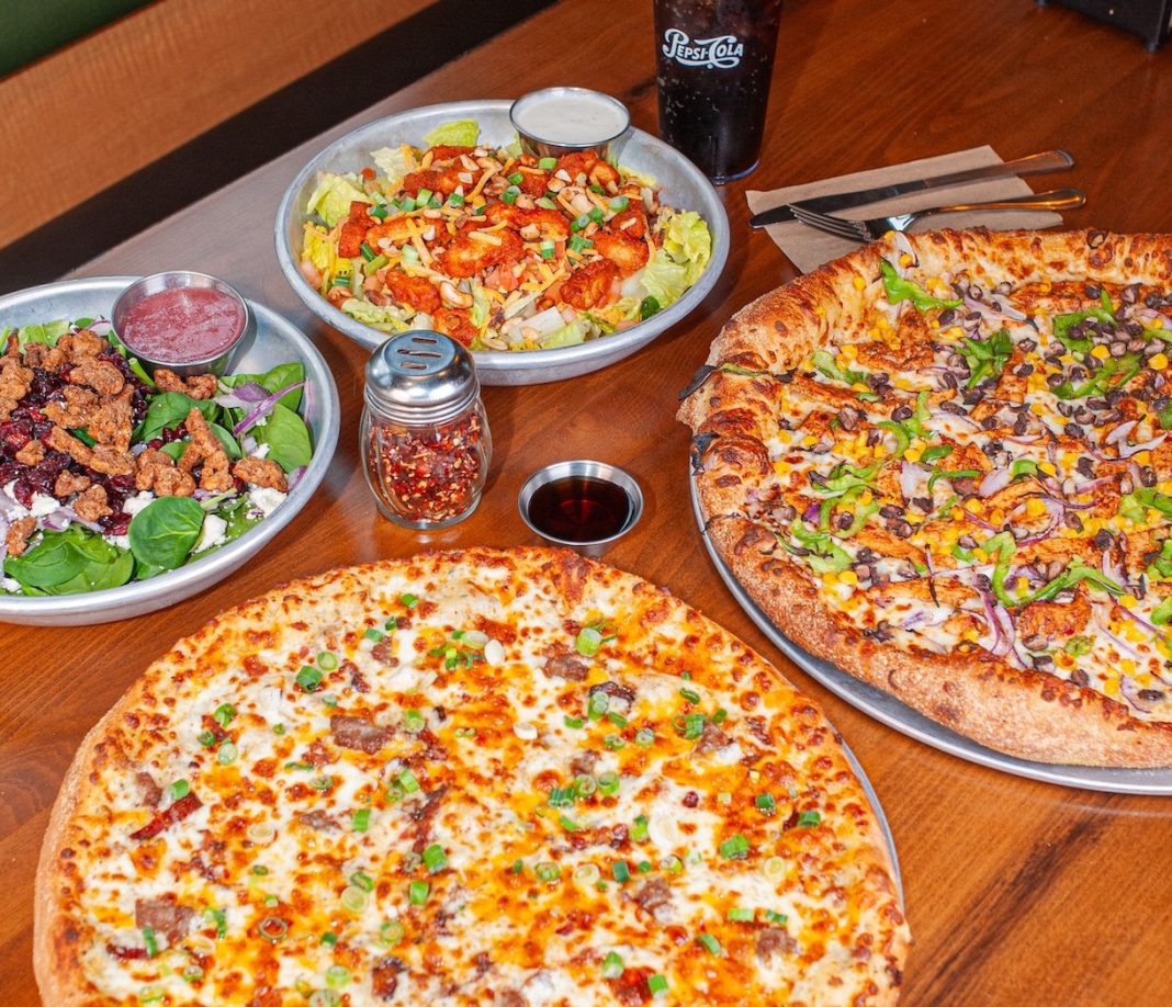 pizzas and salads on a table with a glass of soda