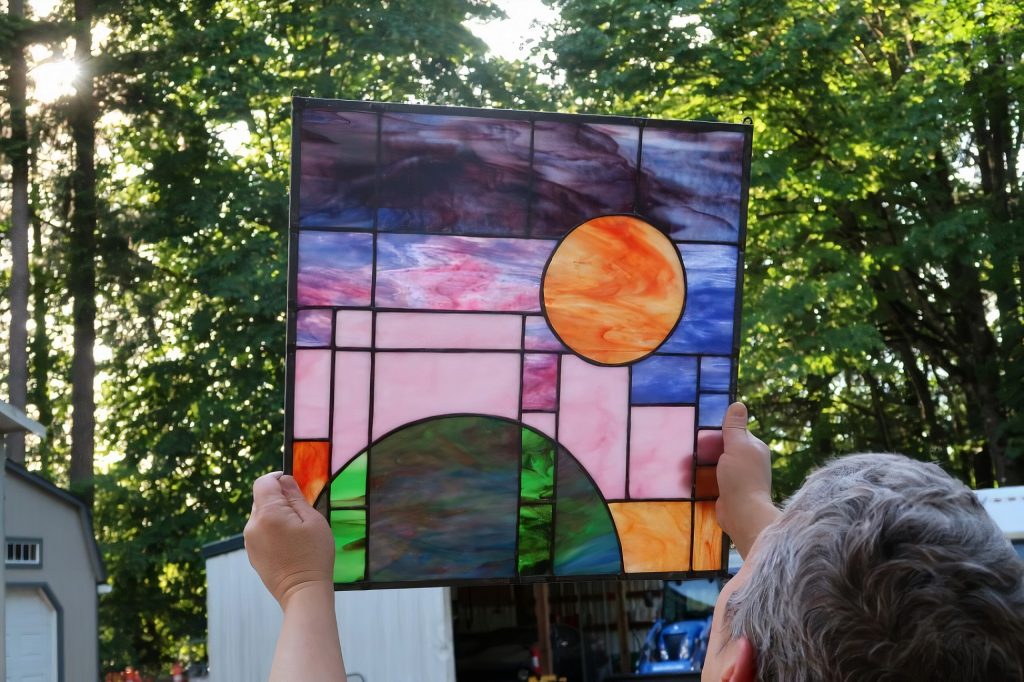 A person holding up a piece of stained glass art featuring different colored rectangles and circles