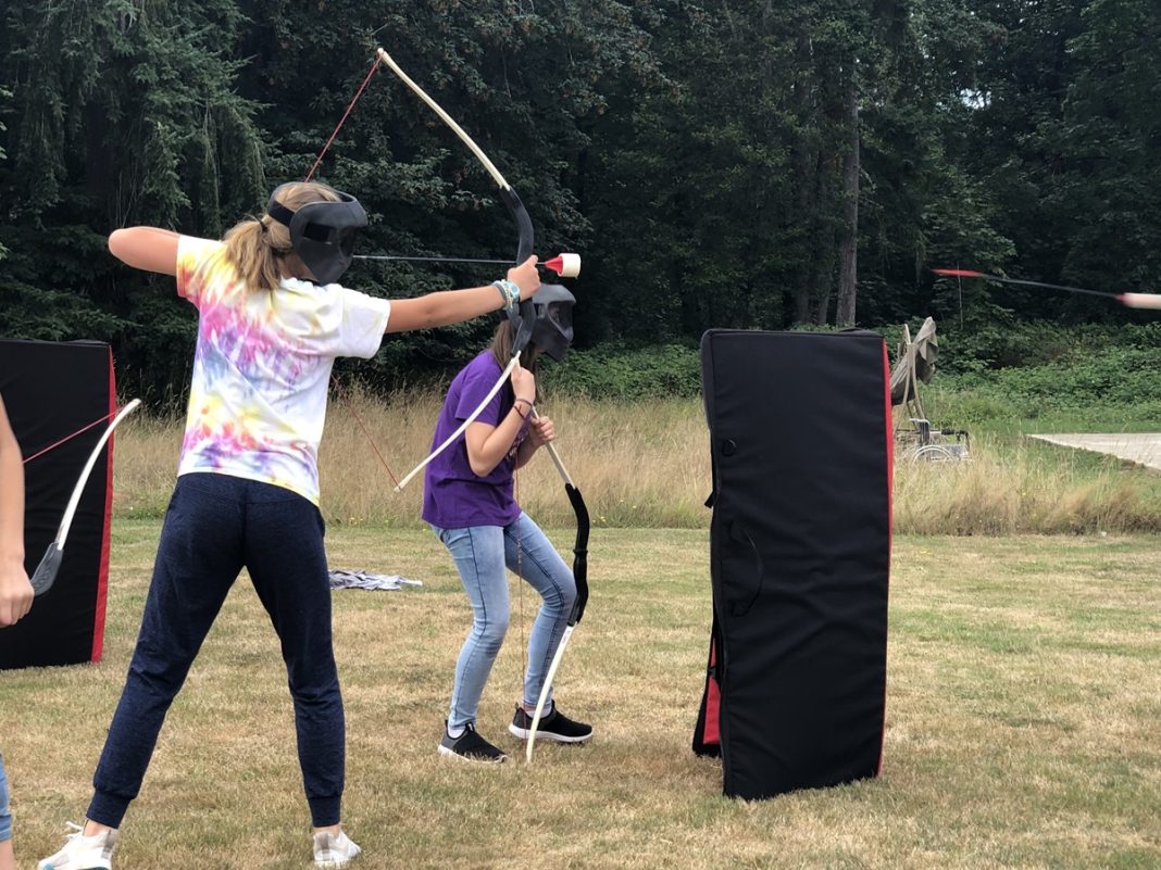 people shooting arrows in a field and hiding behind barriers while playing Extreme Archery Tag