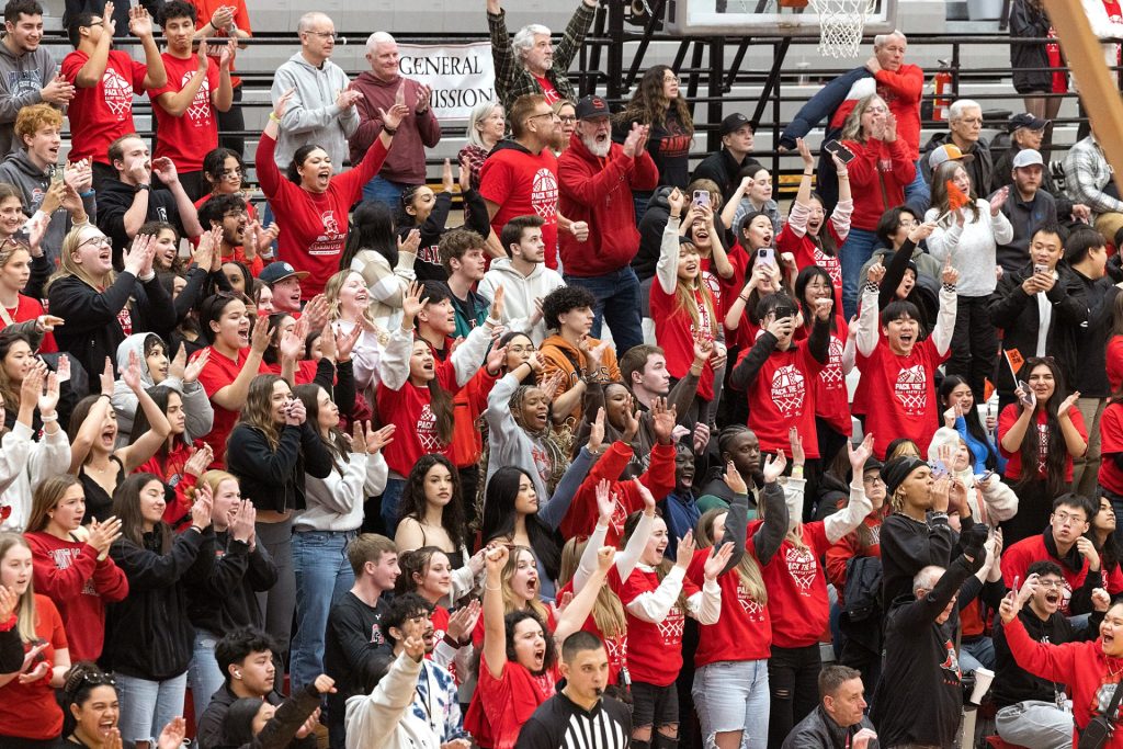 Fans in red and white standing in bleachers at a Saint Martin's University sports game.