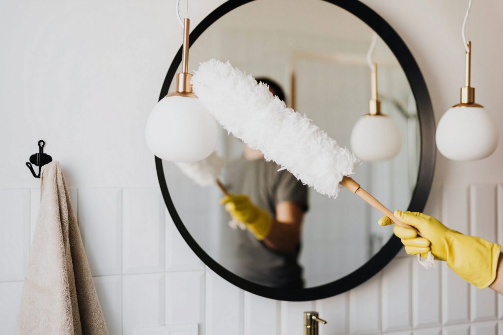 a woman's reflection is seen in a large round mirror she is dusting with a large white feather duster