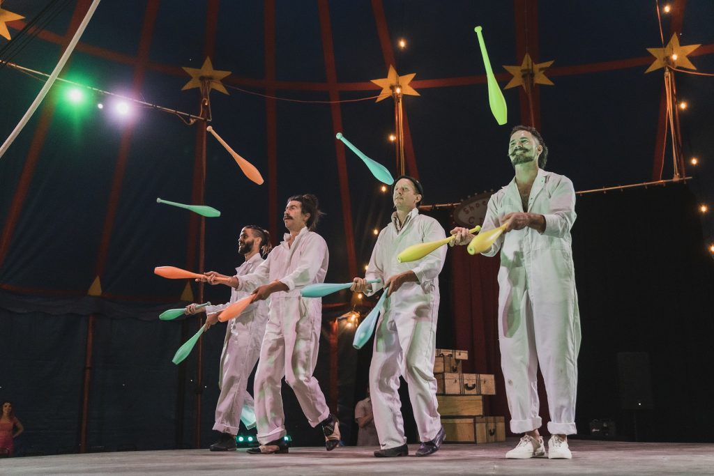 4 men in white jumpsuits juggle on a circus stage for Shoestring Circus