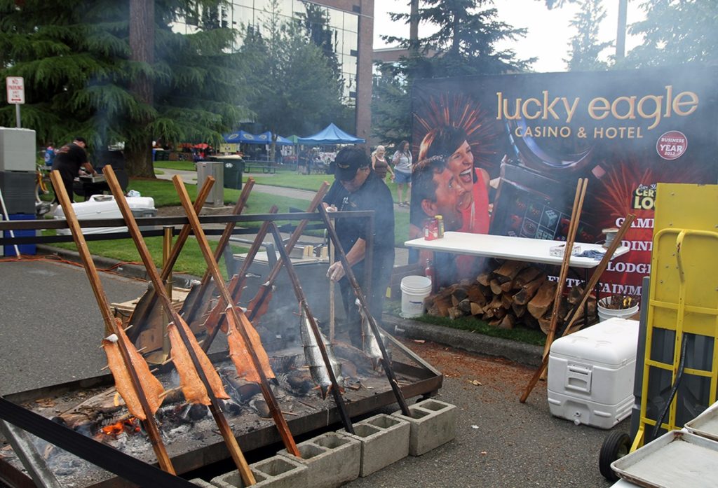 a guy is barbecue salmon on large poles over an open flame at the South Sound BBQ Festival in Lacey, WA