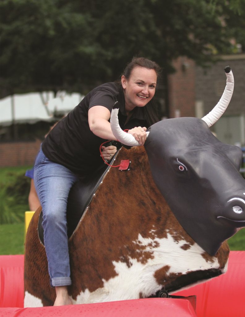 a woman in jeans and a black t-shirt riding a mechanical bull at South Sound BBQ Festival in Lacey, WA