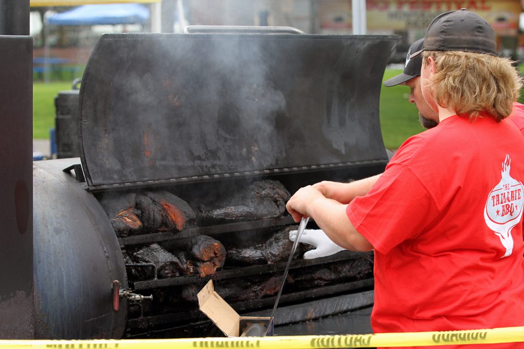 Lady in a red shirt barbecues meat outside on a big black double grill at the South Sound BBQ Fest in Lacey, WA