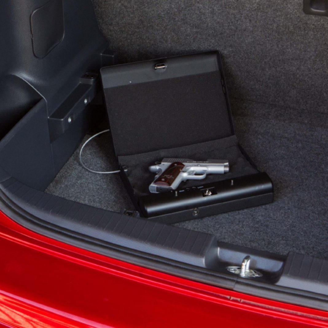 a gun lock box inside the truck of a red car, the box is open and a gun is inside