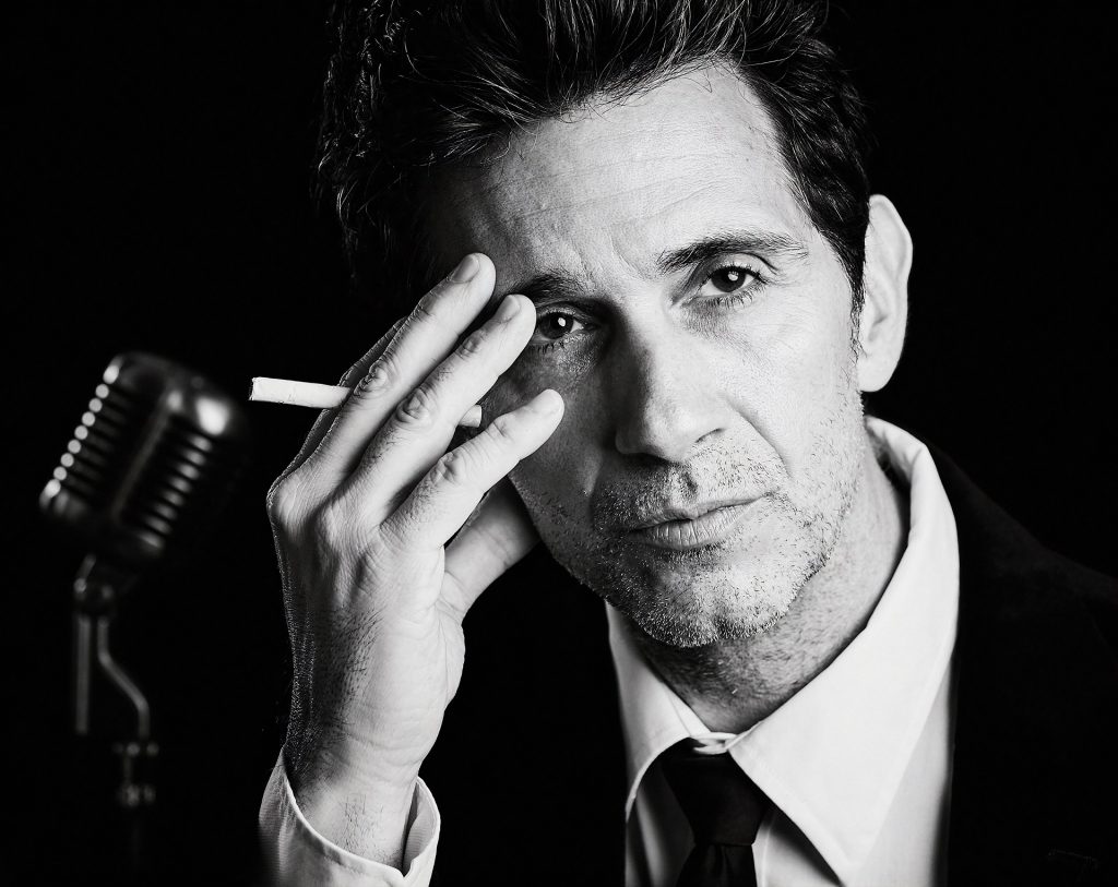 black and white head shot of Ronnie Marmo with a cigarette in his hand he has held up to his face