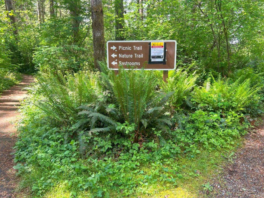a brown sign that says Picnic trail with a right pointing arrow, Nature trail with a left pointing arrow, restrooms with a left pointing arrow