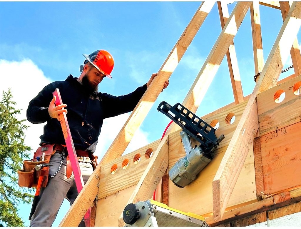 a man in a hard hat stands on platform working on a building frame