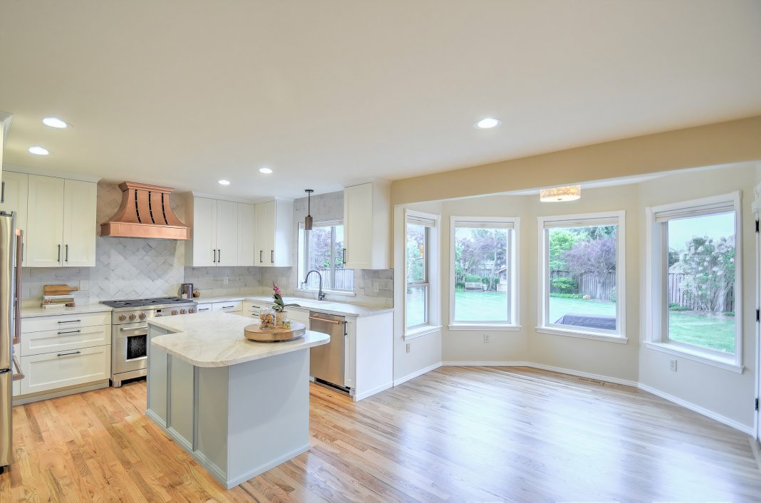 an updated kitchen and dining area with light wood floors, white cabinets and white counters