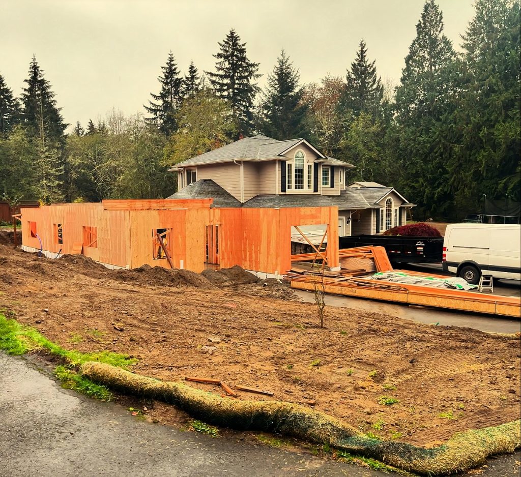 a home being constructed with another home behind it and a line of trees