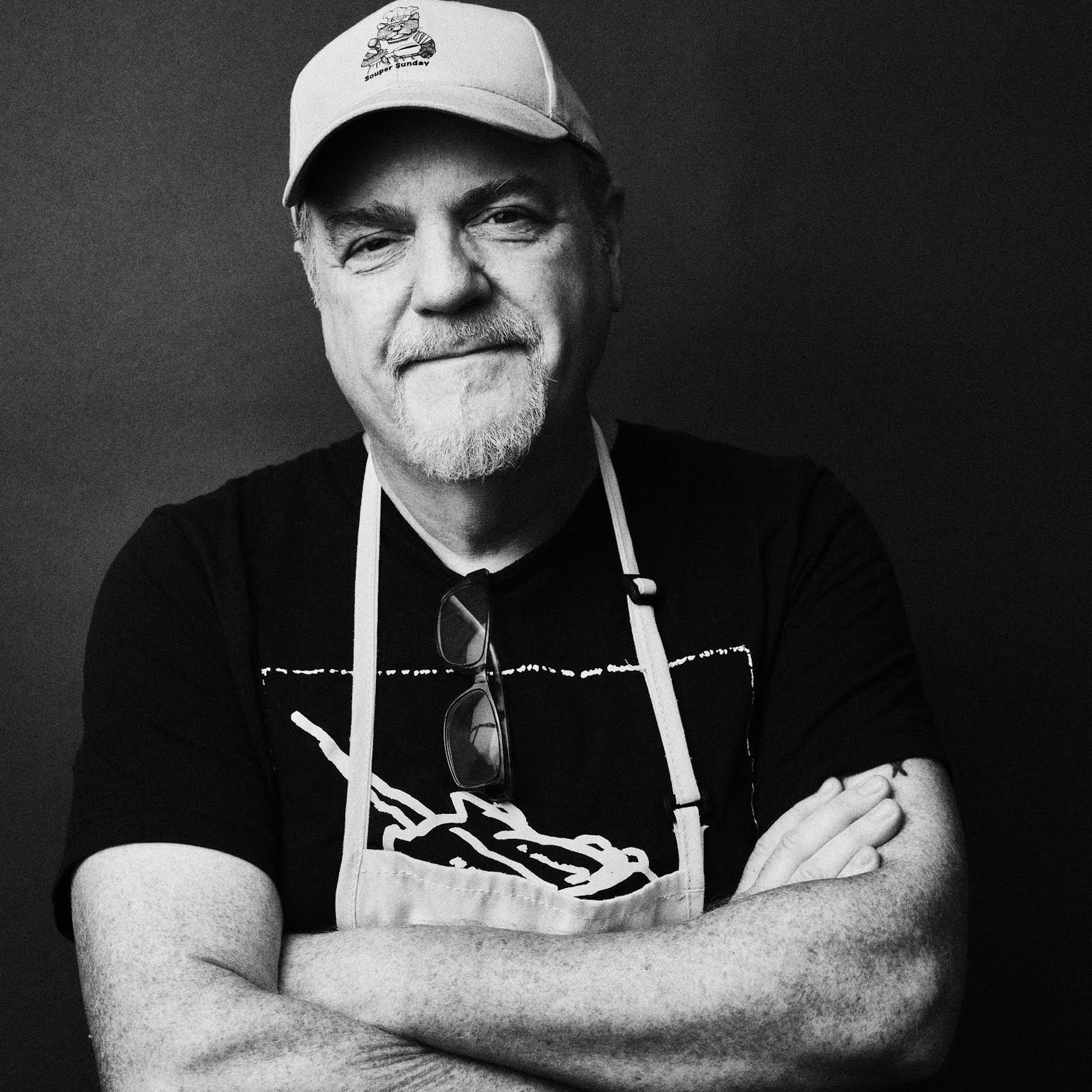 black and white photo of Chris Hyde, wearing an apron with his arms folded across his chest