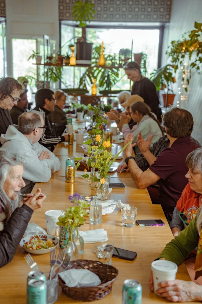 a large group of people sit at several tables pushed together, eating and talking at BITS Cafe