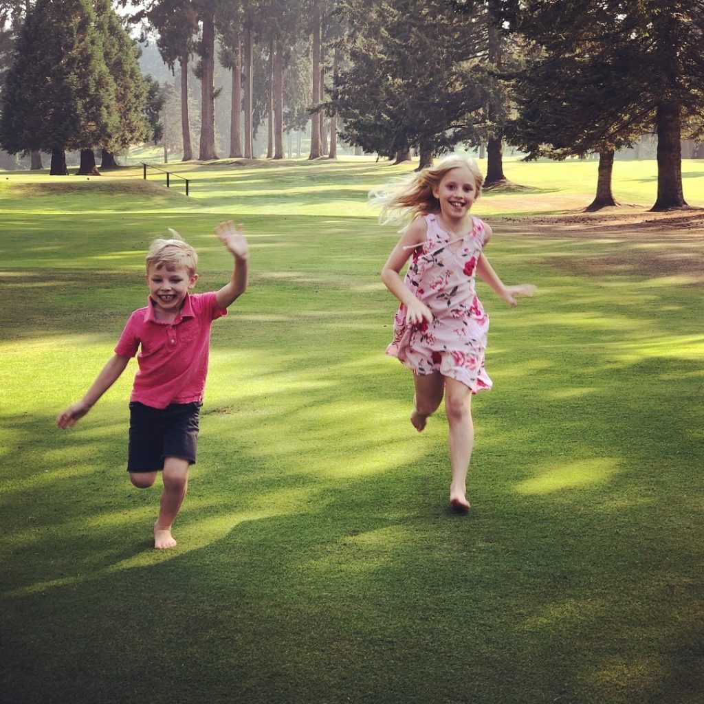 two kids running in a grassy area with trees behind them