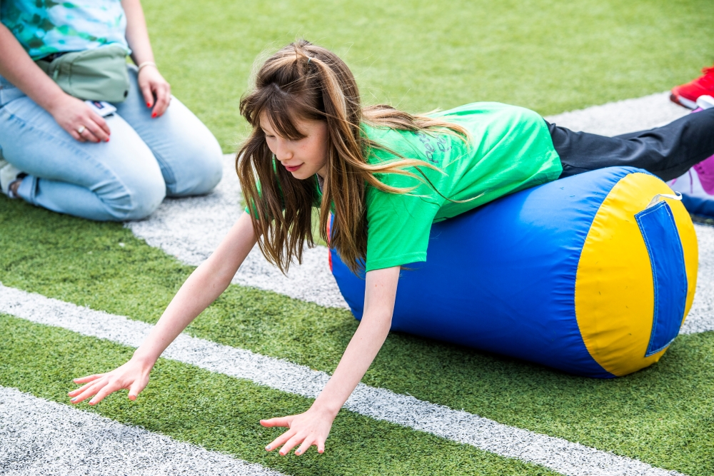 a young girl rolls on her belly on a football field on a large oblong bag at the Day of Champions 2025