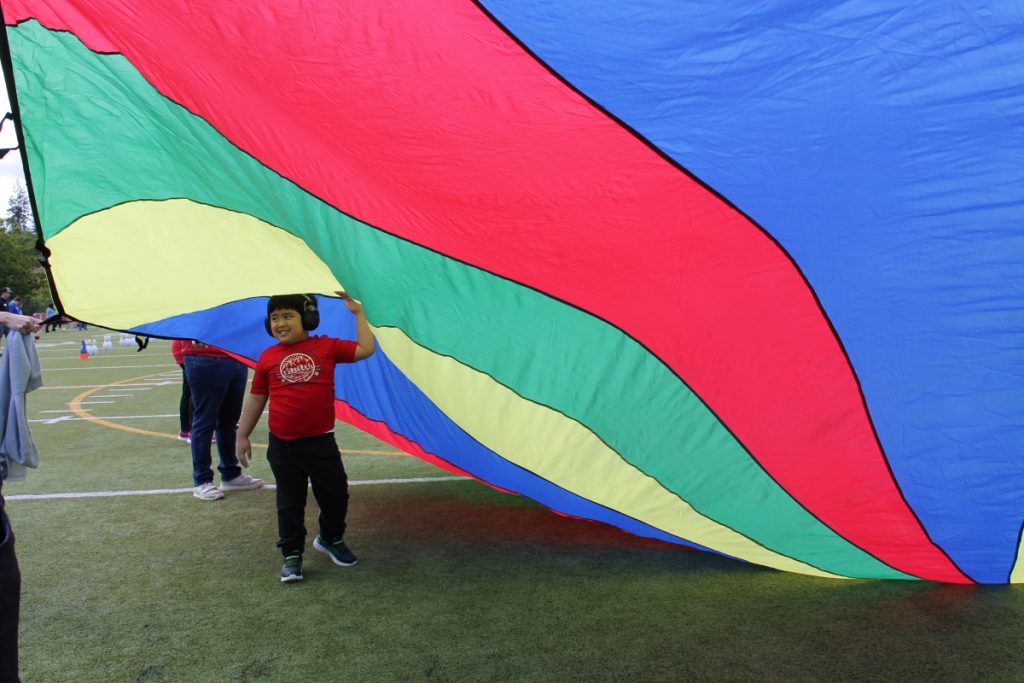 Kids under a giant blue, red, yellow and green parachute at the Day of Champions 2025