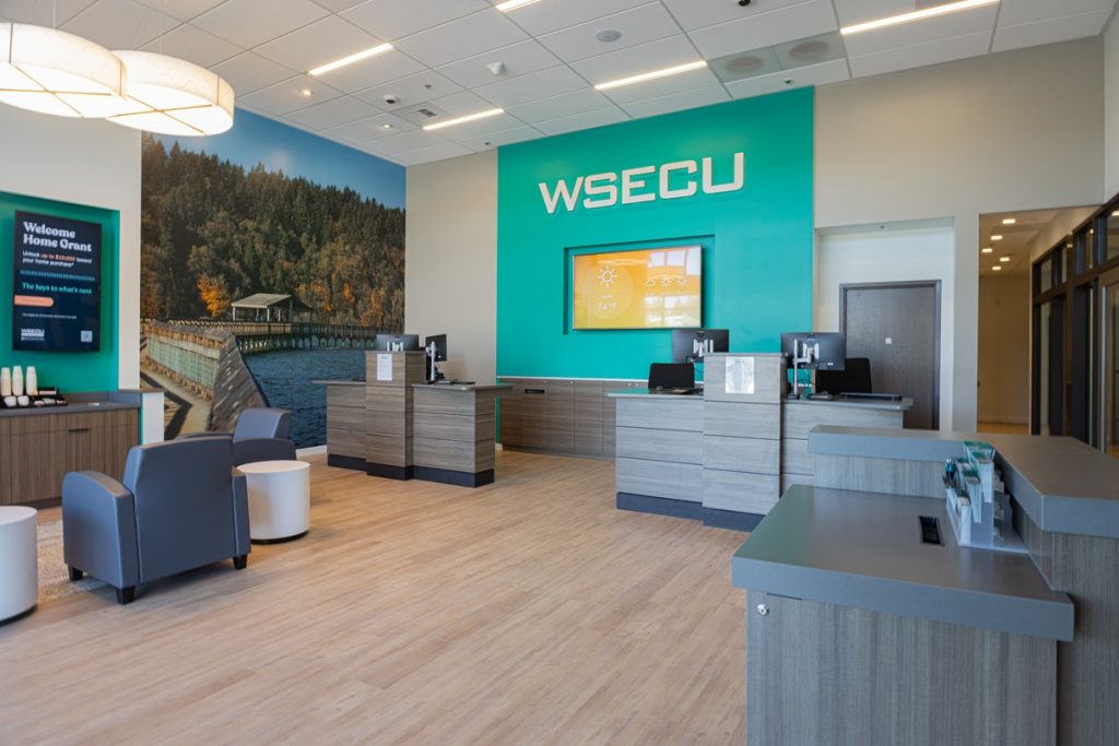 inside of the WSECU Hawks Prairie branch with a teal wall with the text "WSECU" on it, desks, and wood floors