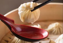 a bowl of bao with a red spoon with broth held over it. A bao is being held above the spoon with chopsticks