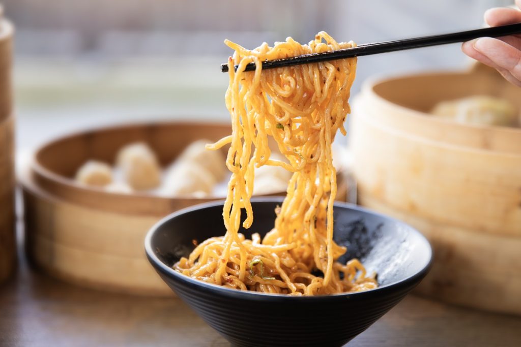 a black bowl full of noodles with some of them being raised up with chopsticks at Dough Zone