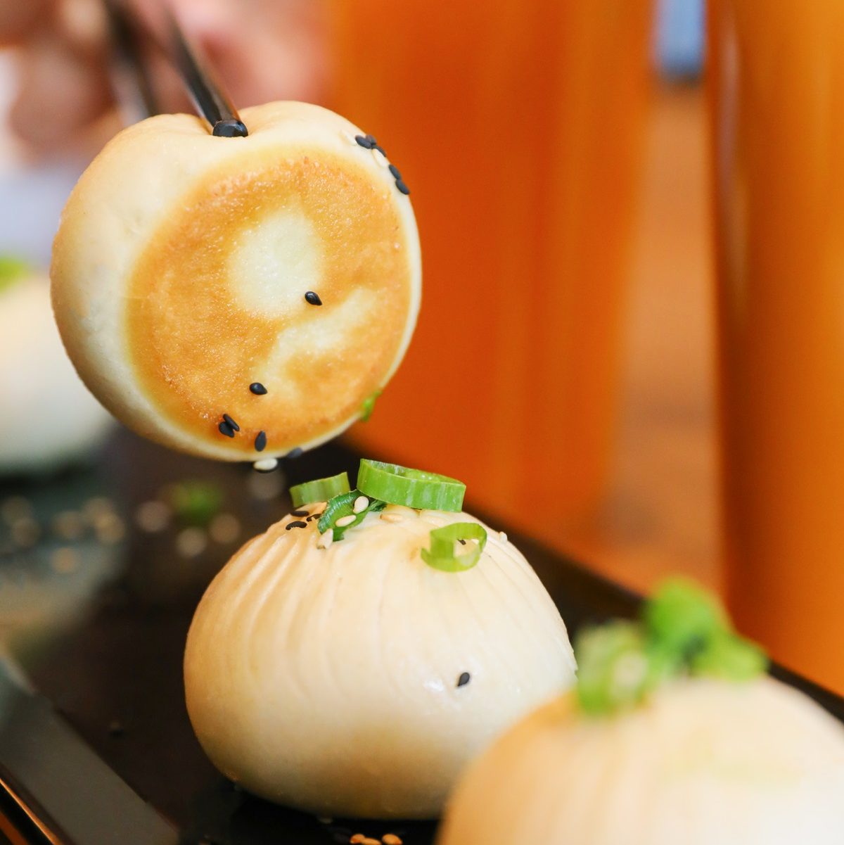 three bao sitting on a black plate, one is being raised up with chopsticks