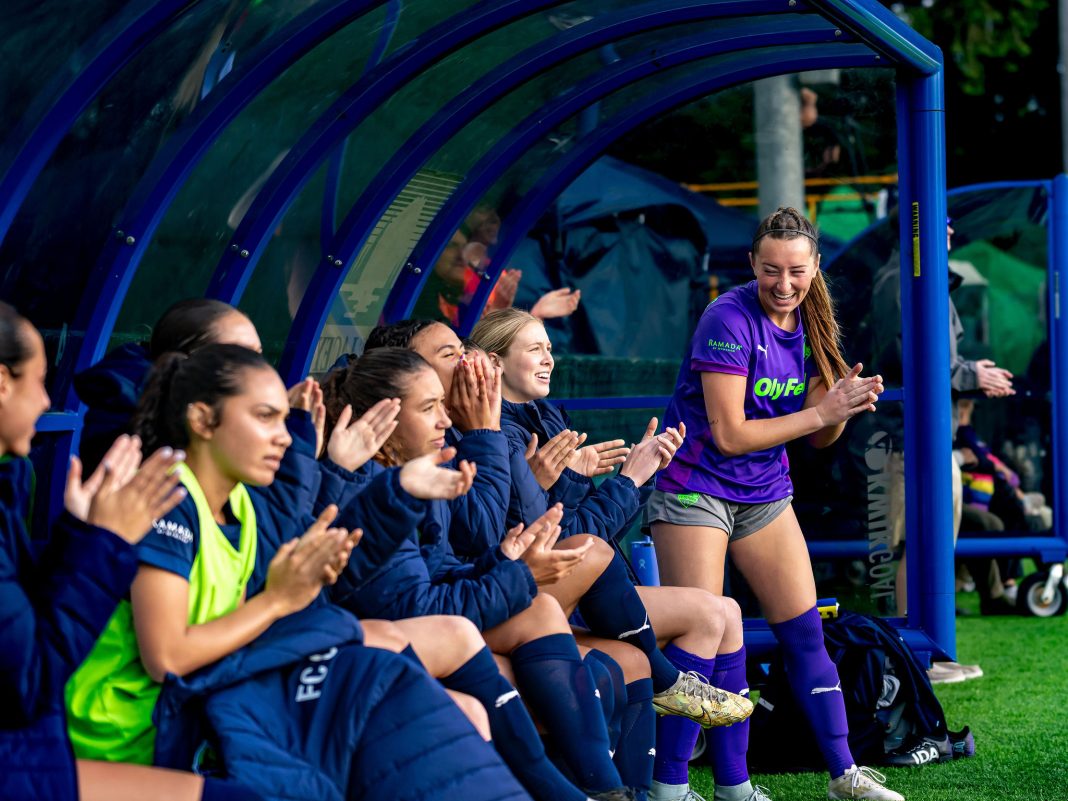 FC Olympia women's soccer team clapping while seated on the bench. one woman is standing